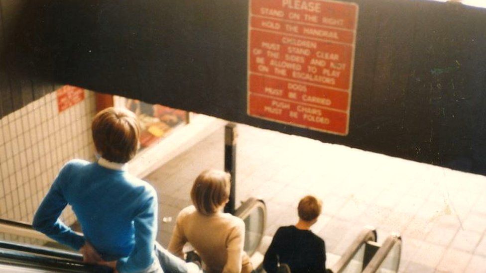 Boys ride the escalators out of Barnsley Market, 1980s