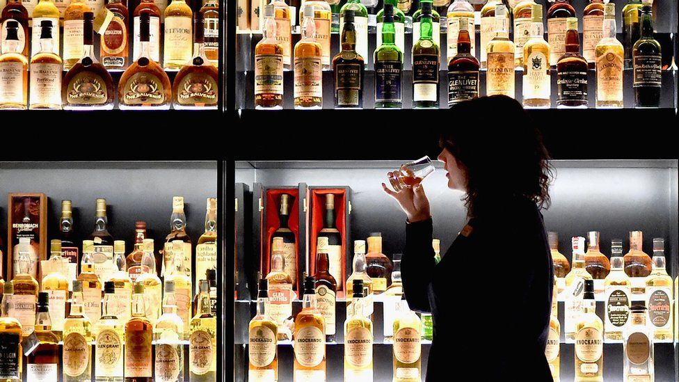 A glass of whisky being sampled against a backdrop of bottles