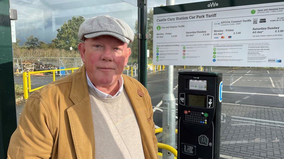 Jeremy Mulford wearing a yellow jacket and a white hat standing in front of the payment shelter at Castle Cary Station car park