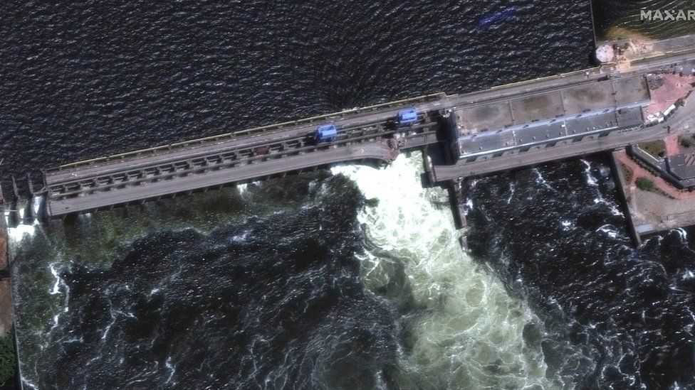An aerial image shows water pouring through what appears to be a breach in the dam