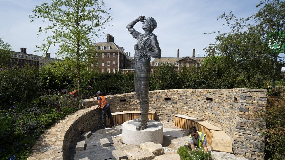 A Chelsea Flower Show garden. with a statue of a man in the centre. being prepared