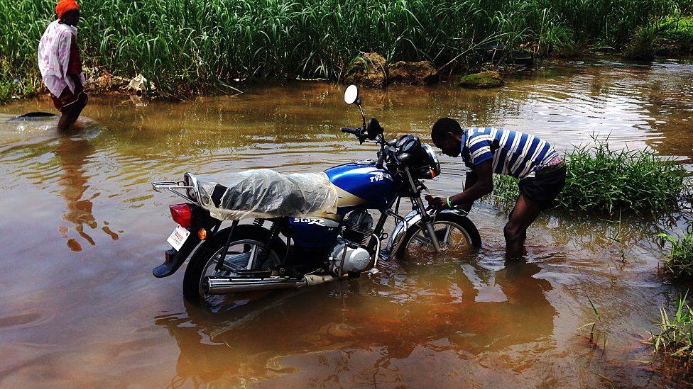 A man washes his motorbike in a flooded road in Liberia