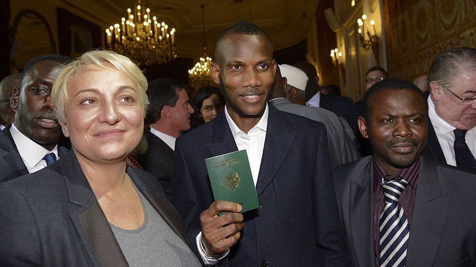 Lassana Bathily (C), a man of Malian origin described as a 'hero' after he helped hostages at a Jewish supermarket hide during last week's Paris attacks holds his French Passport following a ceremony at which was awarded French nationality in Paris on January 20, 2015
