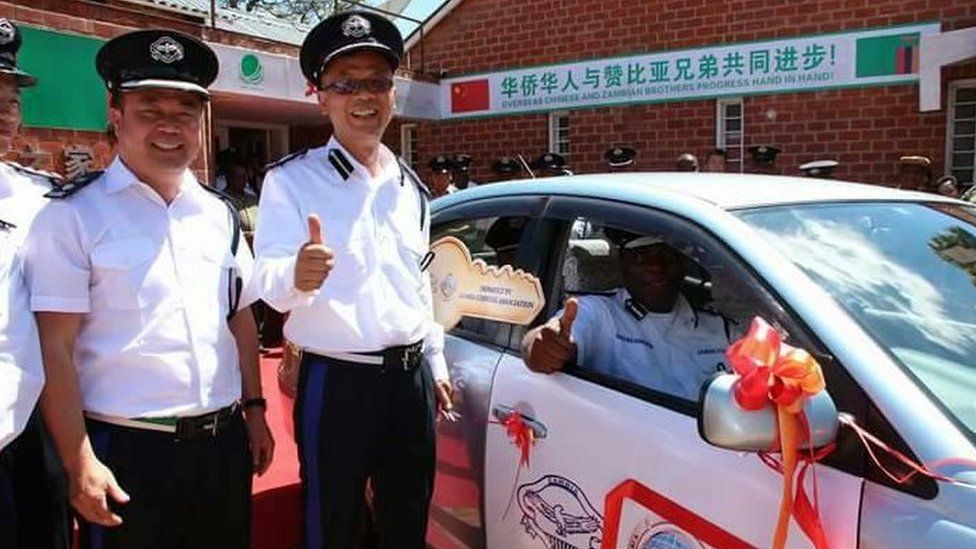 Two Chinese police officers smile alongside a Zambian colleague sitting in a police vehicle