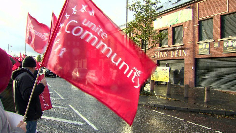 A protester waves a Unite trade union flag outside a Sinn Féin office on Belfast's Falls Road
