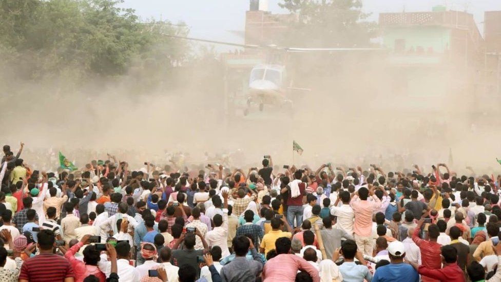 People look on as RJD leader Tejashwi Yadav leaves in a helicopter during an election campaign rally at Masaurhi on October 21, 2020 in Patna