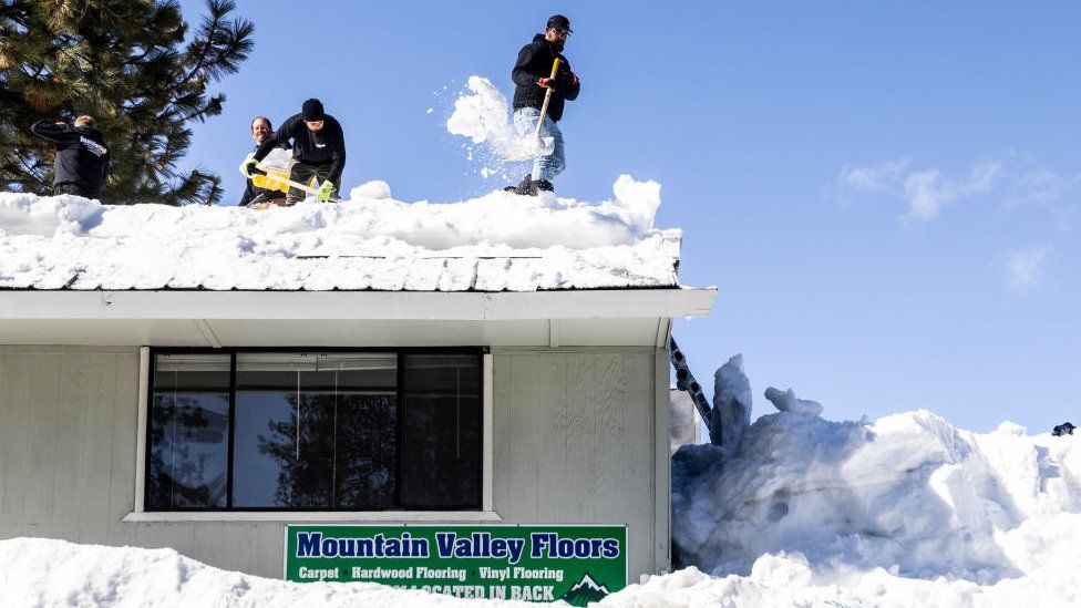 Joey Munoz shovels snow on a roof while he and his coworkers remove snow to avoid further damages to an evacuated building