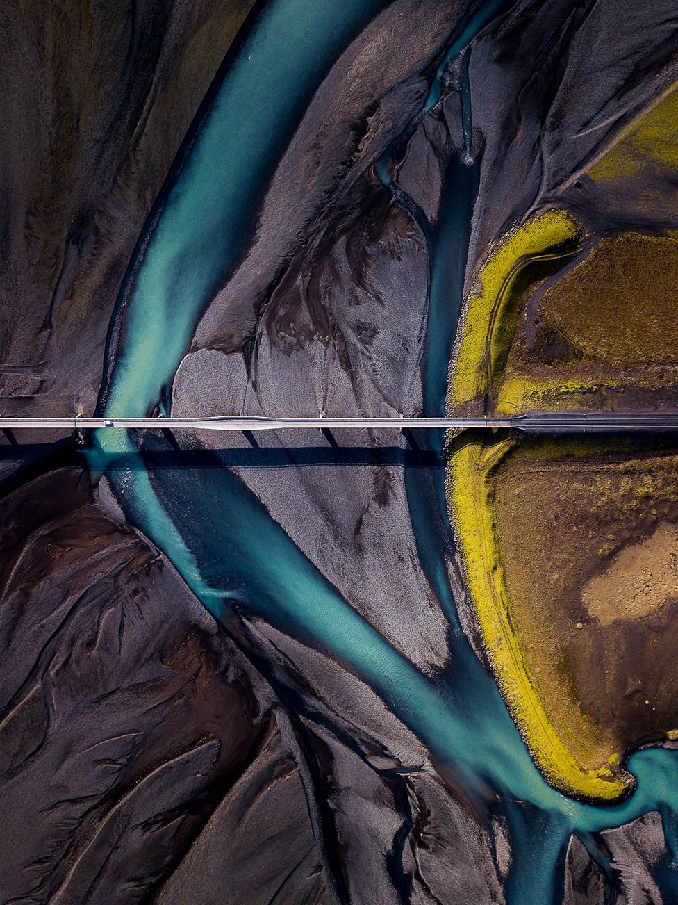 An aerial view of the ground showing dark sand with a blue river cutting through it
