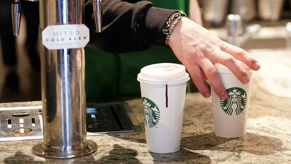 Бариста подает напитки в одноразовых стаканчиках в Starbucks в Лондоне.