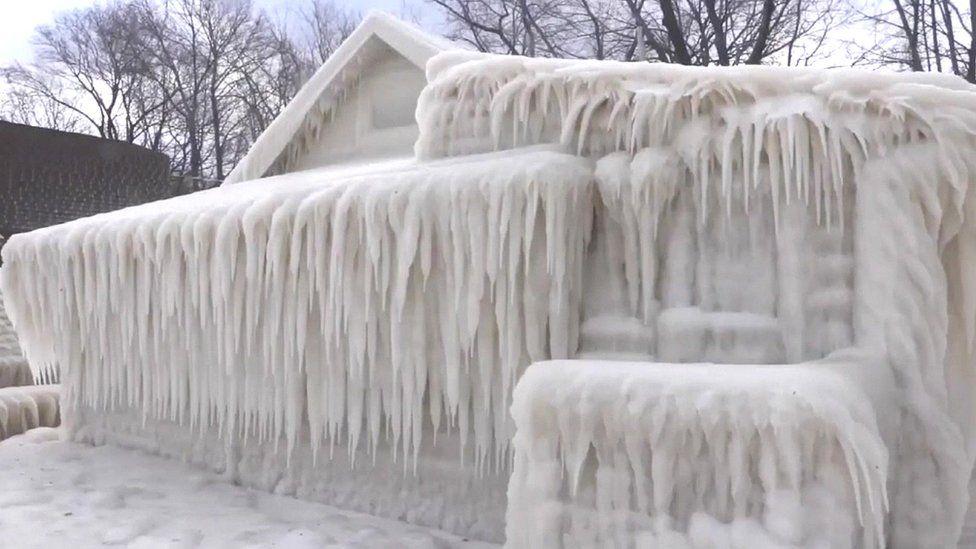 A house is seen completely encased in ice - but still recognisable as a shape - encased in icicles