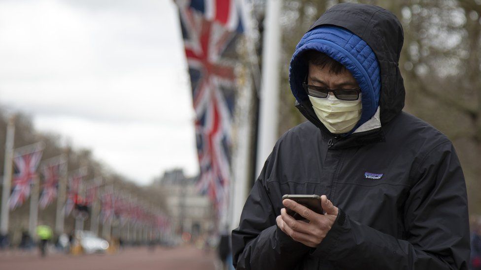 Man wearing a face mask in London with union flags draped on flagpoles in the background
