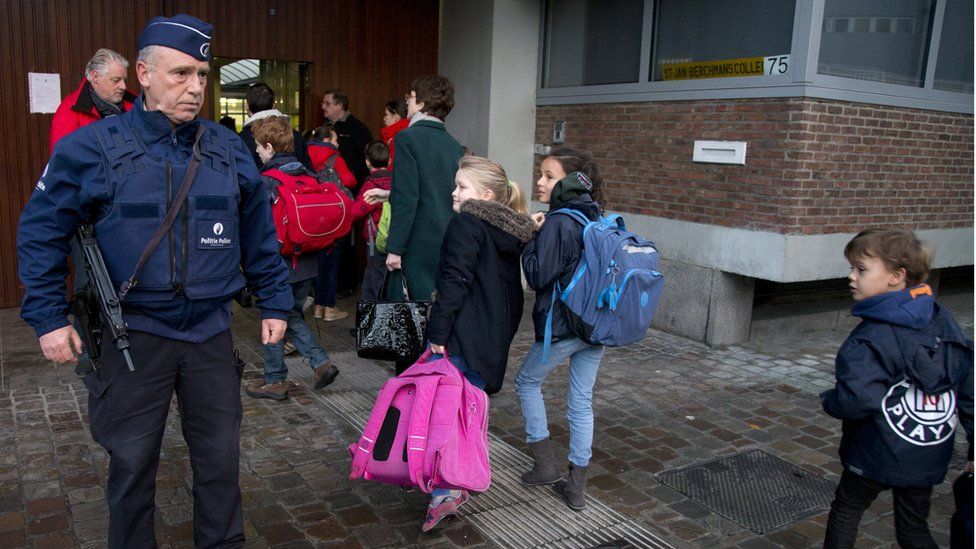 Children pass an armed policeman outside a school in Brussels