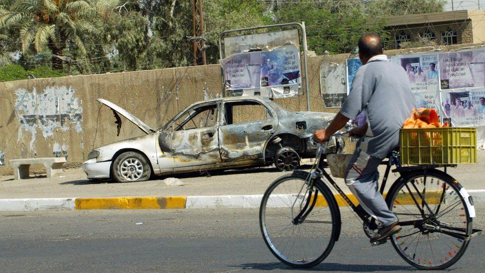 An Iraqi man rides a bicycle passing by a remains of a car burnt during a deadly incident involving Blackwater guards in Baghdad in September 2007