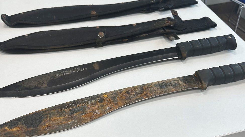 Two large machetes next to their black sheaths