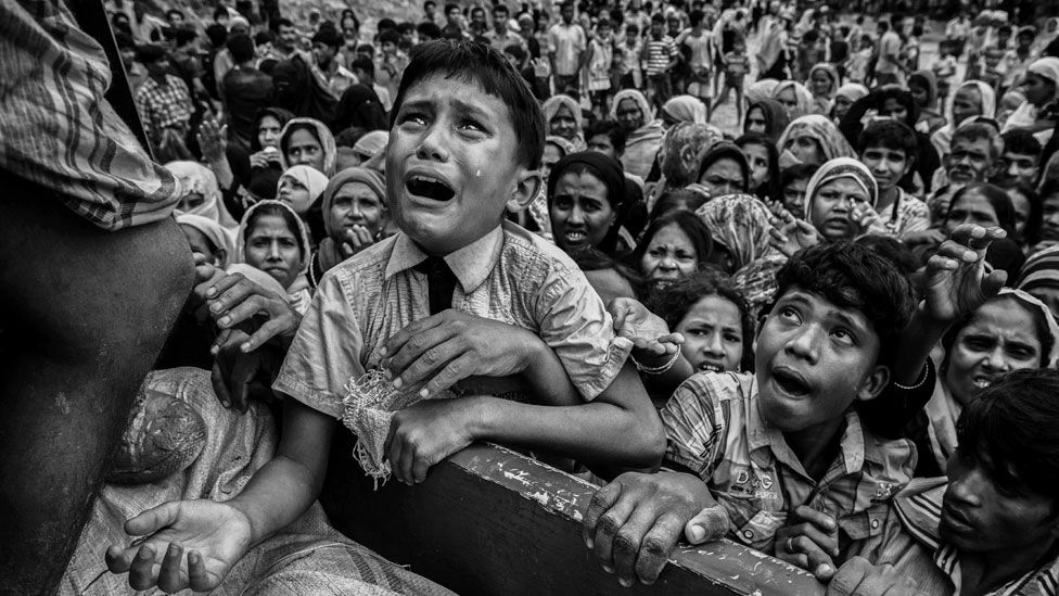 A Rohingya refugee cries as he climbs on a truck distributing aid for a local NGO near the Balukali refugee camp