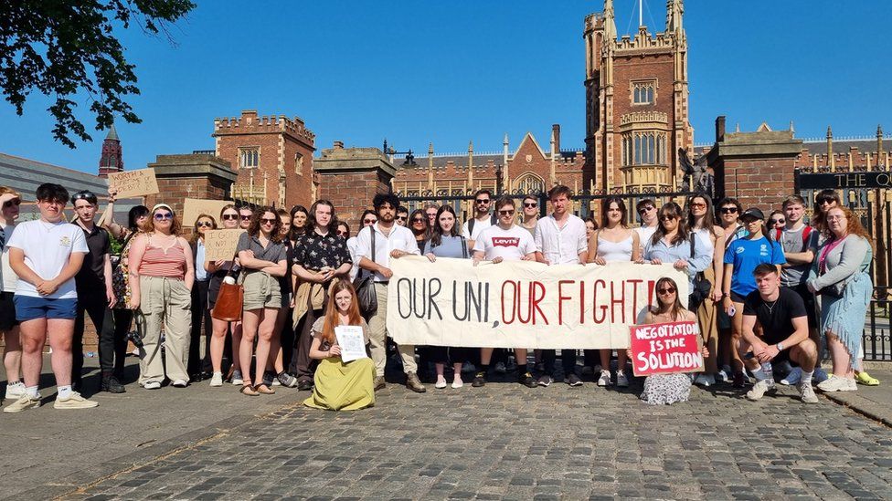 A group of students gathered outside Queen's University Belfast with a sign reading 'our uni, our fight'