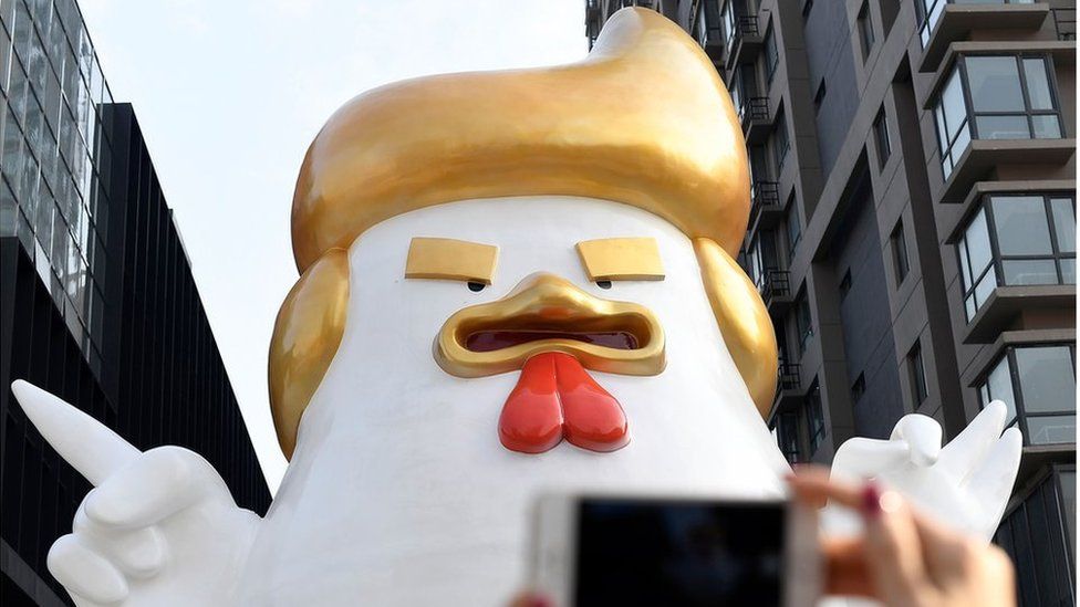A giant rooster sculpture resembling Donald Trump outside a shopping mall in Taiyuan, Shanxi province, with a mobile phone being held by a woman's hands in the foreground. 24 December 2016.
