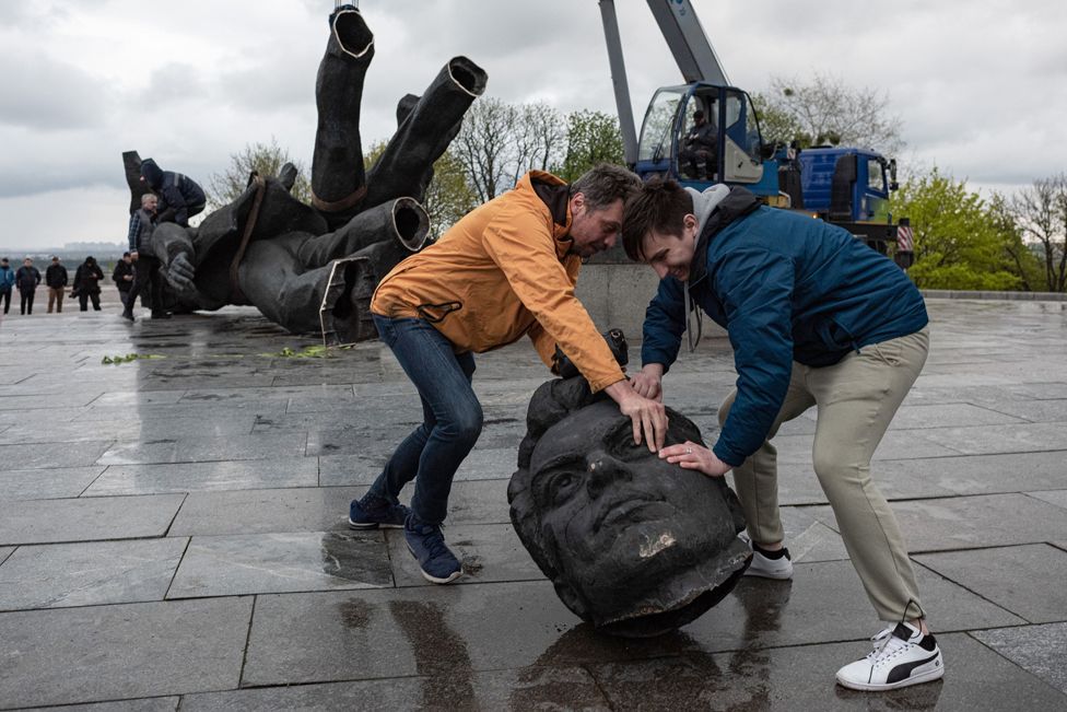 Two men move a head from a statue during its demolition on 26 April 2022 in Kyiv, Ukraine