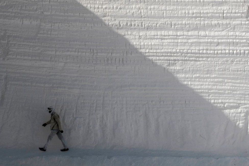 A man walks past a high wall that has been chiselled away.