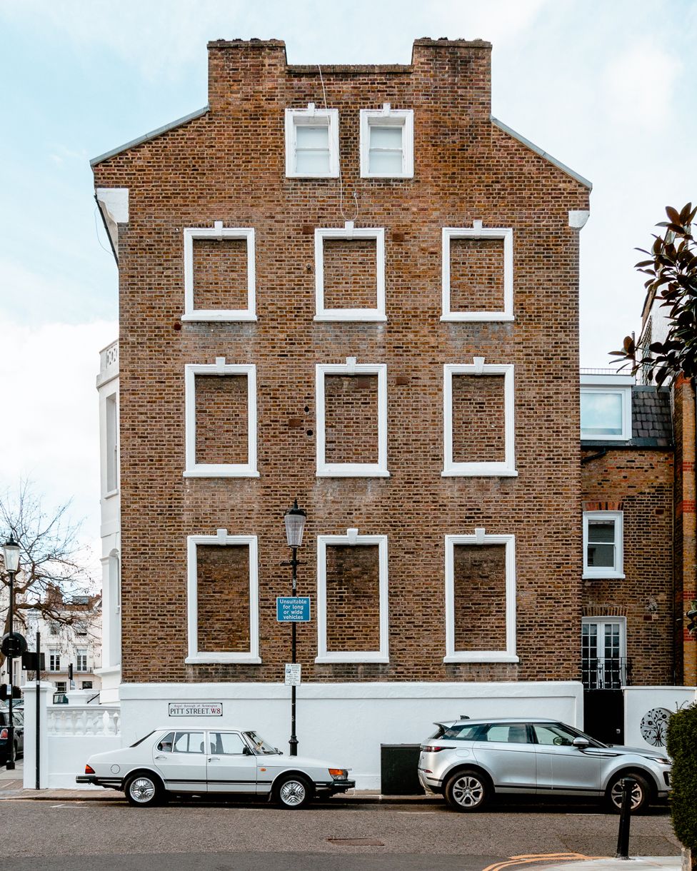 Two cars parked outside of a building with several bricked-up windows, on Pitt Street, London