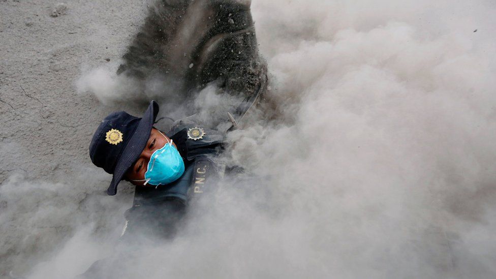 A police officer wearing a blue breathing mask stumbles while running away from a new pyroclastic flow spewed by the Fuego volcano in the community of San Miguel Los Lotes in Escuintla, Guatemala (June 4, 2018)