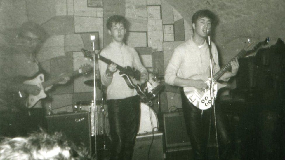 John Lennon and Sir Paul McCartney at the microphone, with George Harrison on guitar and a partially obscured Pete Best, the group's original drummer
