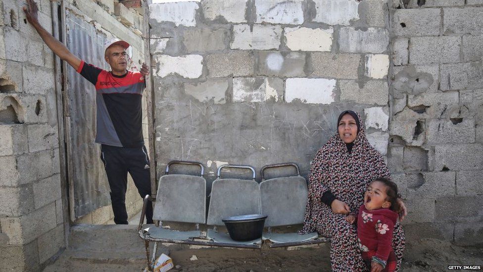 Family pictured outside very basic-looking stone shelter