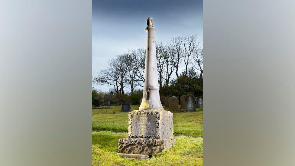 The monument to James Gall and Grace Darling located in Barrow Cemetery. It is shaped like a 10-foot tall lighthouse and features steps leading to a doorway.