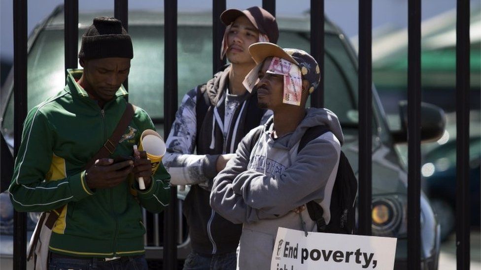 Protesters wear banknotes on their head and placards reading "End poverty, job losses and inequalities", during a Cosatur march to the parliament in Cape Town, on 5 October 2015