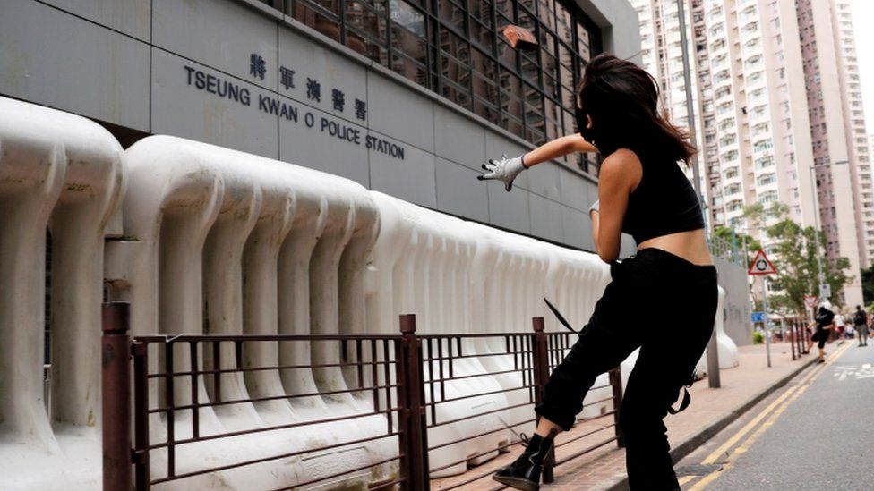 A woman throws a rock at a police station in Hong Kong