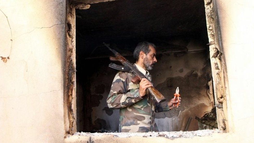 A fighter loyal to Libya's internationally recognised government checks a damaged house in Benghazi after seizing the centre of the eastern coastal city (23 February 2016)