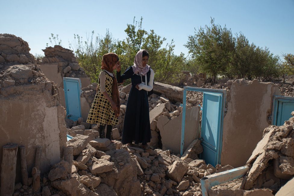 Two girls search in the debris for the remains of their homes at Siah Ab