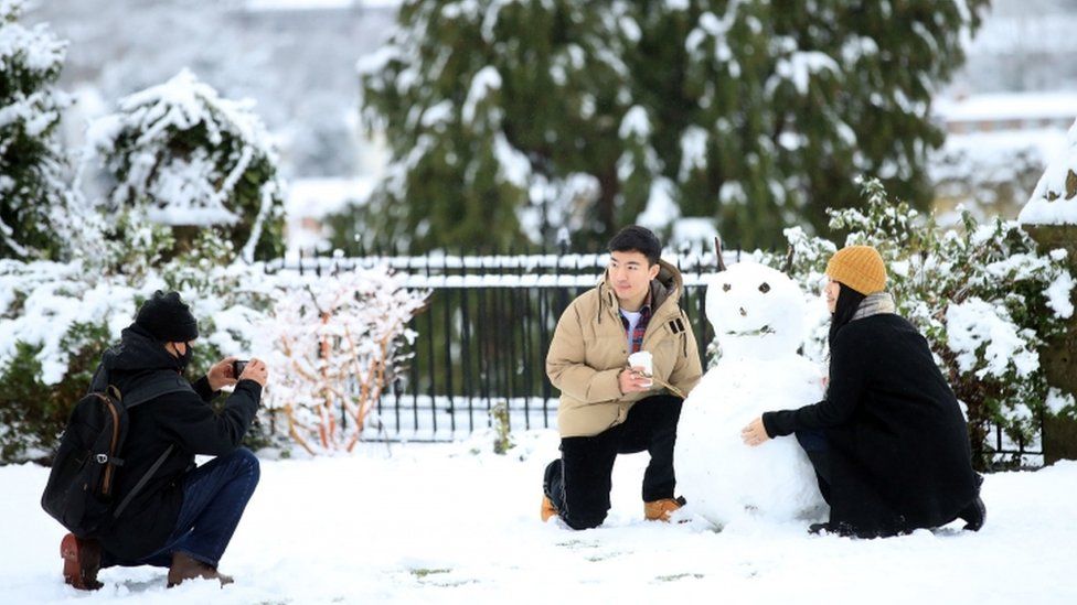 People pose next to a snowman in the grounds of Guildford Castle, Surrey