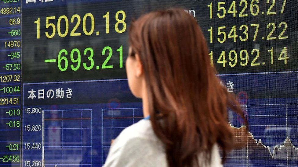A pedestrian walks past a share prices board showing numbers of the Tokyo Stock Exchange in Tokyo on February 12, 2016