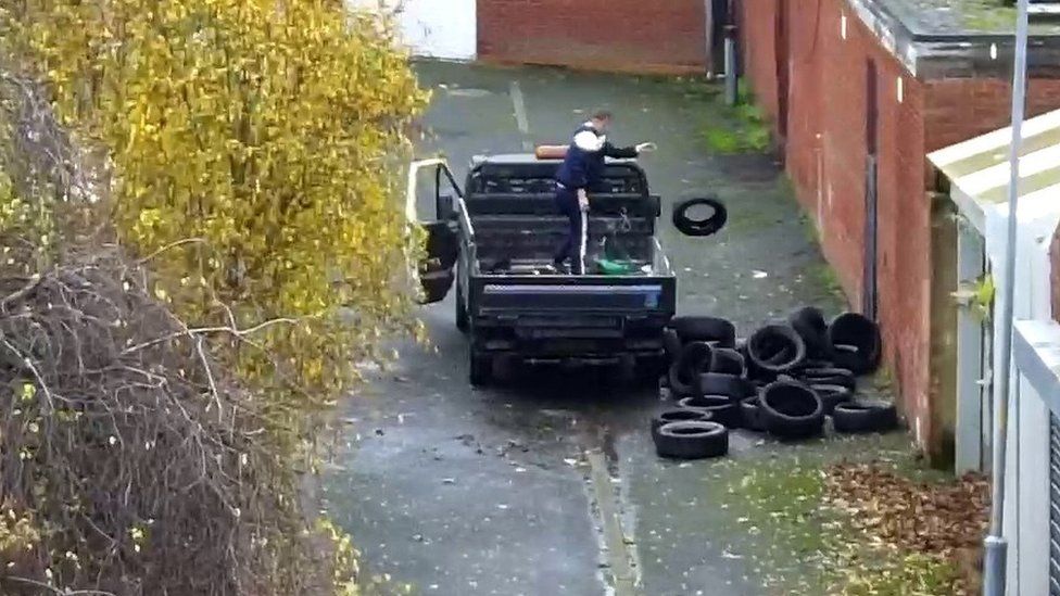 CCTV camera still of one men on a truck loaded with tyres, throwing one on to the ground where other tyres are piled up