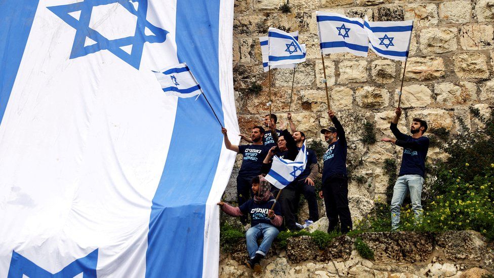 Demonstrators drape a large Israeli flag on a wall of Jerusalem's Old City as the government presses on with its controversial judicial overhaul (23 March 2023)