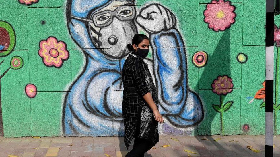 A pedestrian walks past a wall mural depicting frontline Covid-19 coronavirus warriors wearing face masks along a road in New Delhi on March 21, 2021