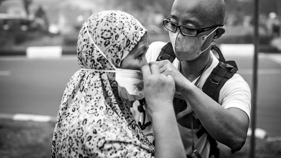 A volunteer helps a woman in Indonesia's Kalimantan province to put on a specialised N95 mask