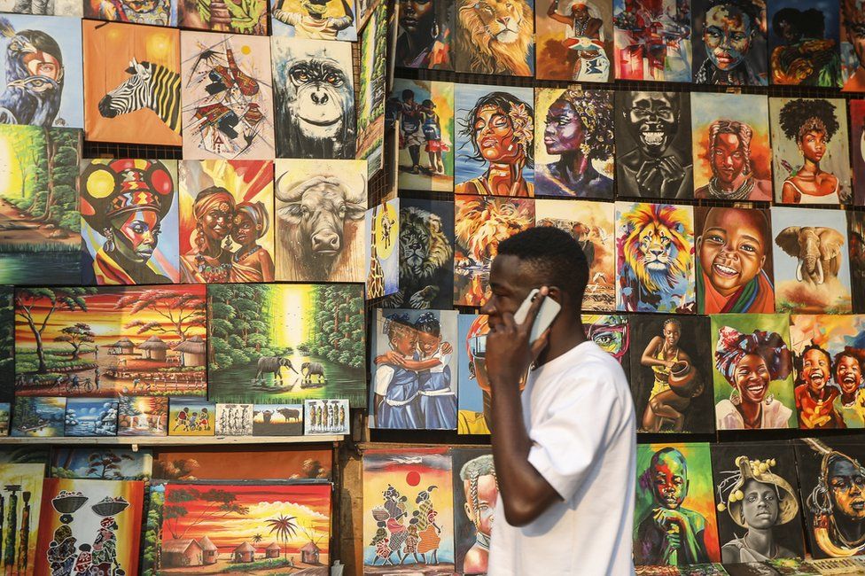 A man walks past different paintings on display for sale.