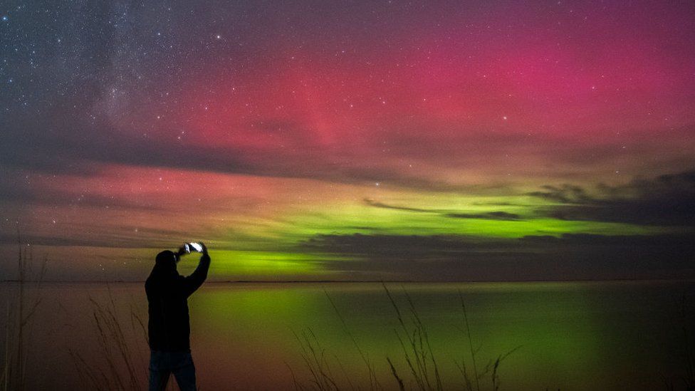 Мужчина фотографирует северное сияние над озером Селвин в районе Кентербери Новой Зеландии