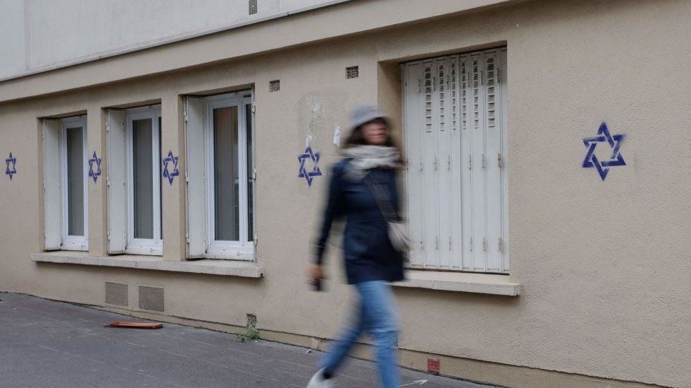 A woman walks along a building whose facade is covered with Stars of David in Paris