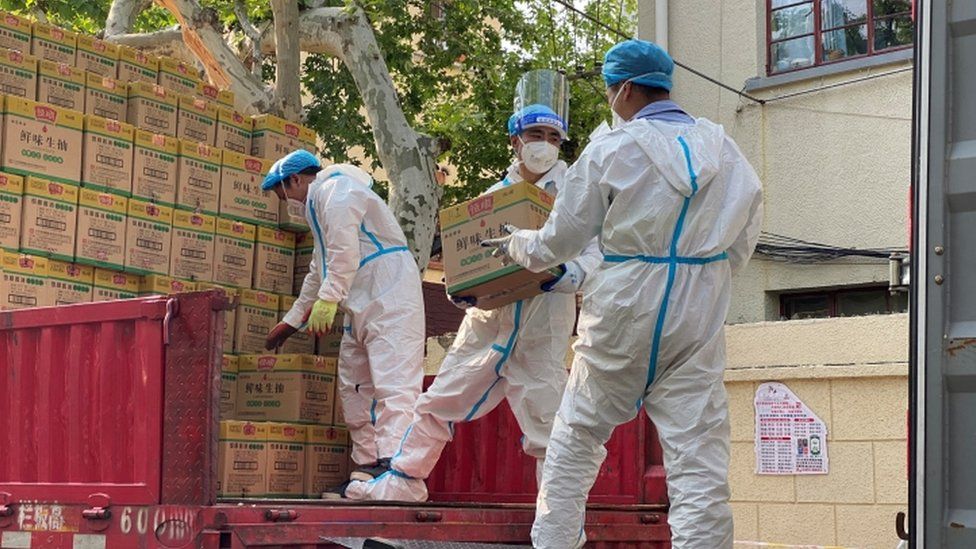 Image shows workers in hazmat suits unloading boxes