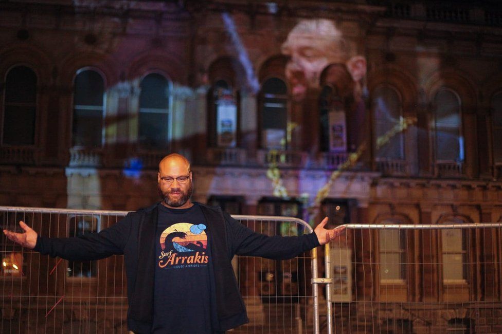 Glen Chisholm in front of a projection of him in Ipswich