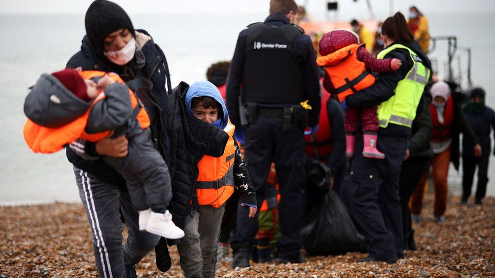 Migrants walk along a beach after being brought to shore by the RNLI at Dungeness