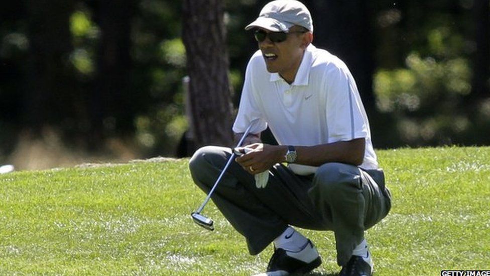 President Barack Obama squats by a golf course green.