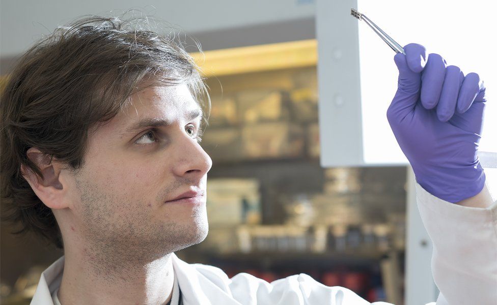 PhD student Kenny Marshall holds up a piece of perovskite solar cell