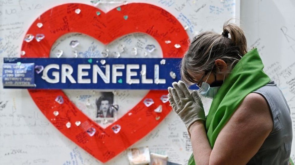 A woman stands near the Grenfell memorial wall