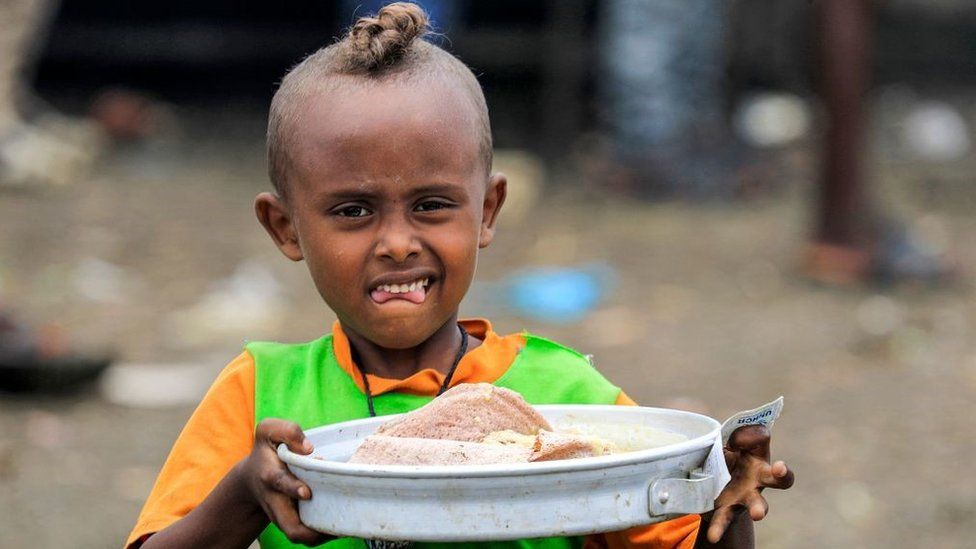 A child walks with a tray carrying soup and traditional Injera Ethiopian sour flatbread as Ethiopian refugees of the Qemant ethnic group queue for food at a camp in the village of Basinga in Basunda district of Sudan's eastern Gedaref region on August 10, 2021.
