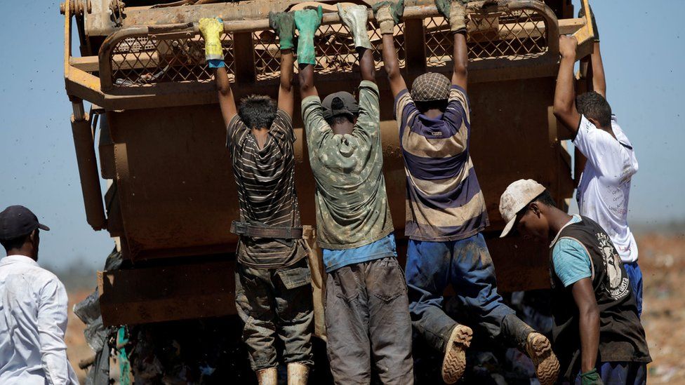 Youths hang from a rubbish lorry at Lixao da Estrutural, Latin America's largest rubbish dump, in Brasilia, Brazil, 19 January 2018