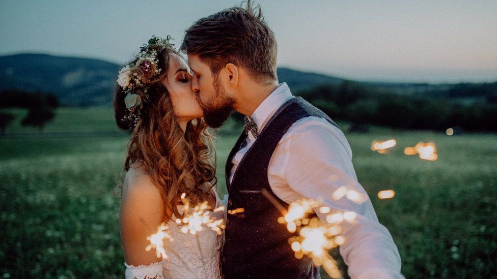 A man and a woman at their wedding holding sparklers in a field